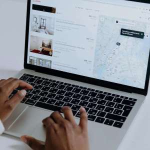 Hands typing on laptop searching Airbnb for accommodation options with map view.